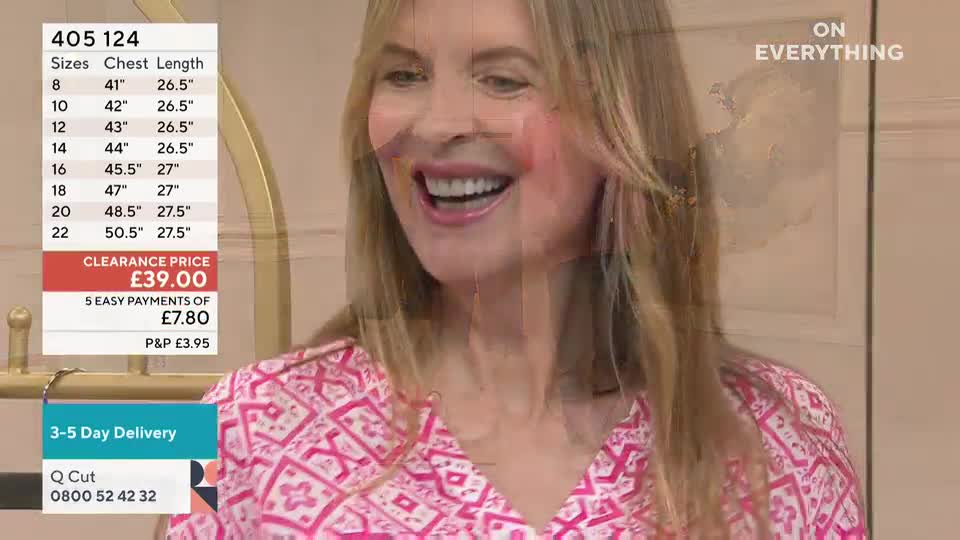 A woman in a patterned pink top grins widely, her face lit up. Beside her, a screen displays the price and size information for a garment, typical of a QVC-style presentation.
