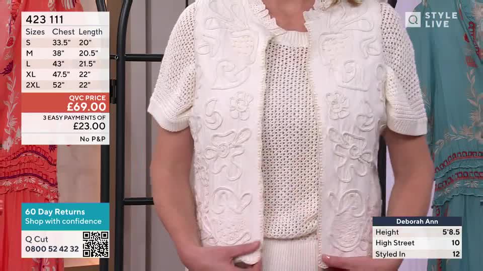 A woman in a cream-colored, embroidered jacket stands facing the camera. She's demonstrating the garment on a QVC-style show, with a price tag displayed on the screen.

