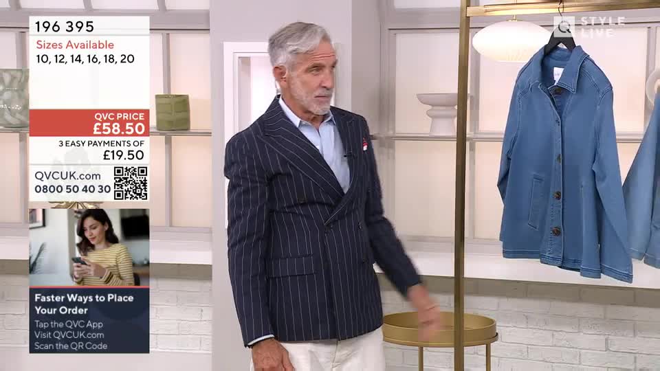 The man in the pinstripe blazer gestures toward a denim jacket hanging on a rack. A QVC price and ordering information are displayed on the left side of the screen.
