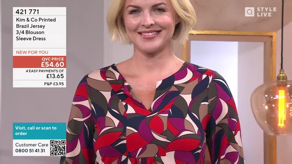 A woman in a patterned dress smiles directly at the camera, likely in a QVC studio.  The price of the dress, £54.60, is displayed on a graphic to the left.
