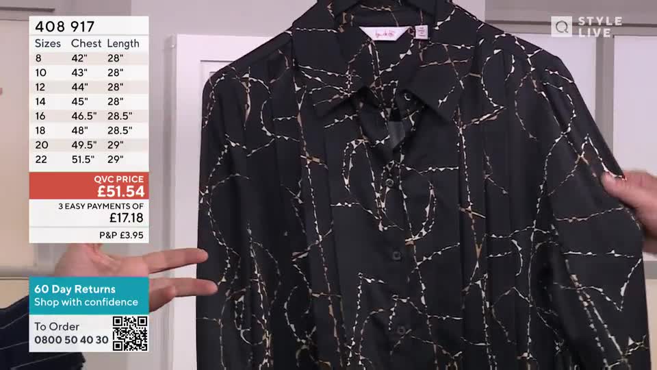 A presenter holds up a black shirt patterned with a gold-colored design, showing off the fabric on QVC Style Live. The price and sizing details are displayed on the screen.
