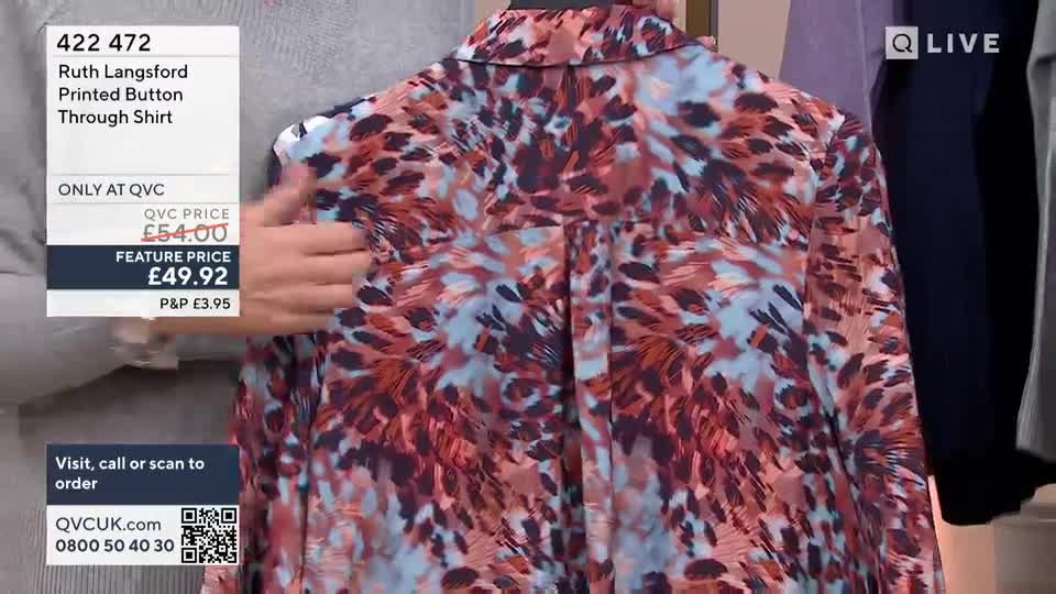 A hand is holding up the back of a patterned shirt, showing off the fabric's design on a QVC segment. The presenter is pointing out the details of the garment.
