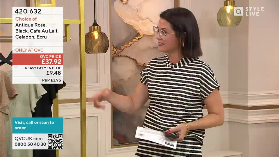 The woman in the striped top gestures towards a rack of clothing, holding a small remote in her other hand. A screen displays the price and color options of the featured item, all presented in the style of a QVC broadcast.
