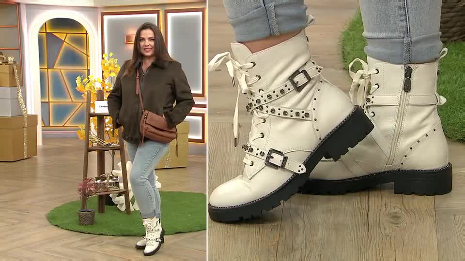 The woman in the studio is showcasing white, buckled boots with studded straps. She's wearing a brown jacket and jeans, standing in a brightly lit, QVC-style setting.
