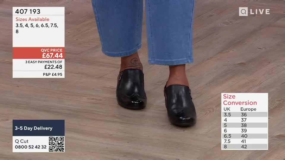 A person's feet are moving slowly, showcasing shiny black shoes with a small decorative pattern on the toe. The camera angle is focused on the feet, and the background shows details about the product and pricing, typical of a QVC-style broadcast.
