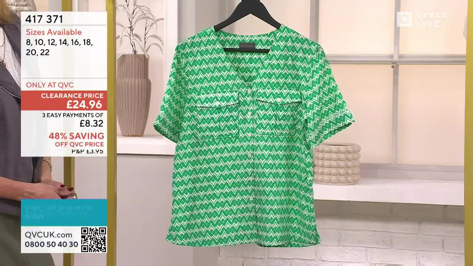 A green patterned blouse hangs on a black hanger against a neutral backdrop. The QVC screen displays the price and sizes available for the item.
