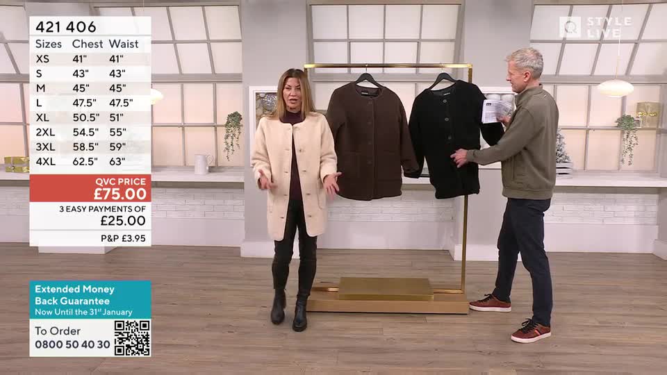 A woman in a cream coat gestures towards a rack where two other coats hang. A man in a green jacket holds up the black coat, showing a tag.
