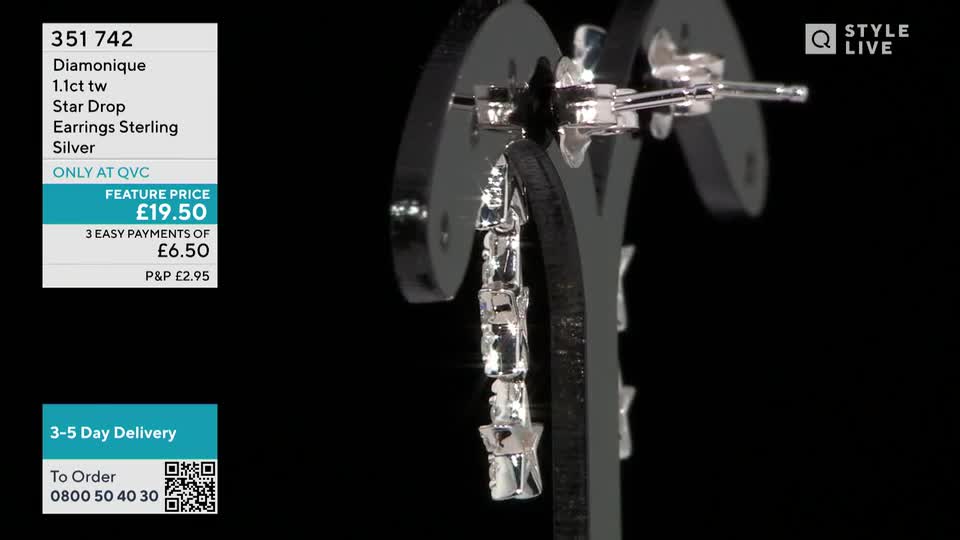 A pair of dangling earrings, sparkling with what looks like cubic zirconia, hangs from a black display stand. The QVC price tag is visible in the corner, offering them for under twenty pounds.
