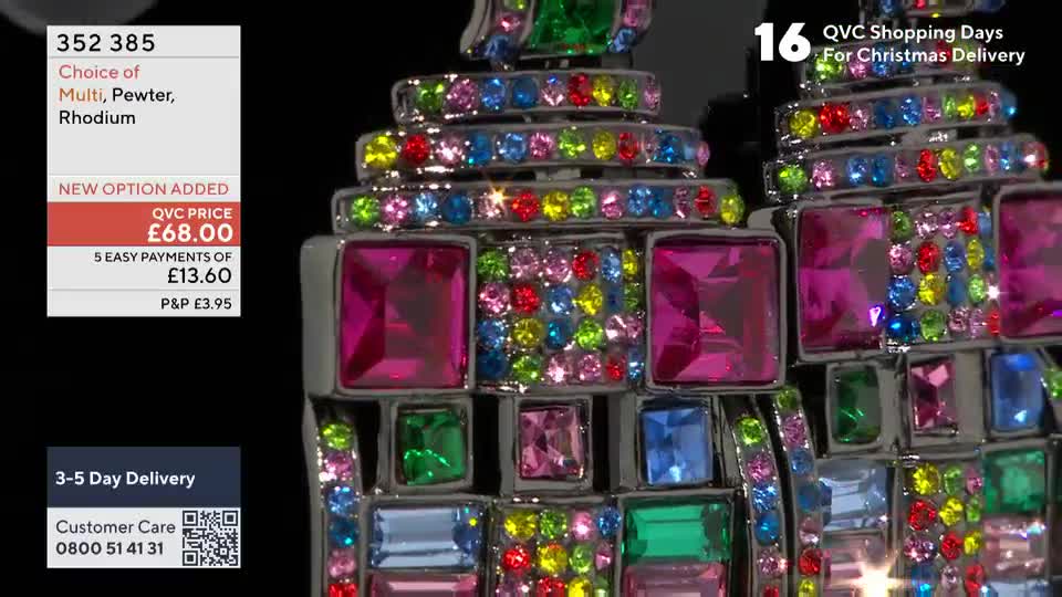 A pair of large, bejeweled earrings, looking like miniature buildings, are on display. The camera focuses on the colorful, sparkling stones, with a price tag and QVC details in the background.
A pair of large, bejeweled earrings, looking like miniature buildings, are on display. The camera focuses on the colorful, sparkling stones, with a price tag and QVC details in the background.