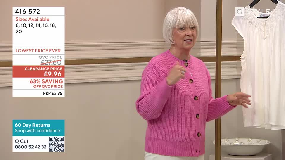 A woman in a bright pink cardigan gestures enthusiastically as she talks. Beside her, a crisp white blouse hangs on a display stand.