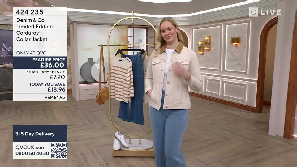 A woman in a cream corduroy jacket and blue jeans stands on a polished wooden floor, gesturing with her hands. Nearby, a rack displays a striped top and a denim skirt, with a tan crossbody bag hanging from it.