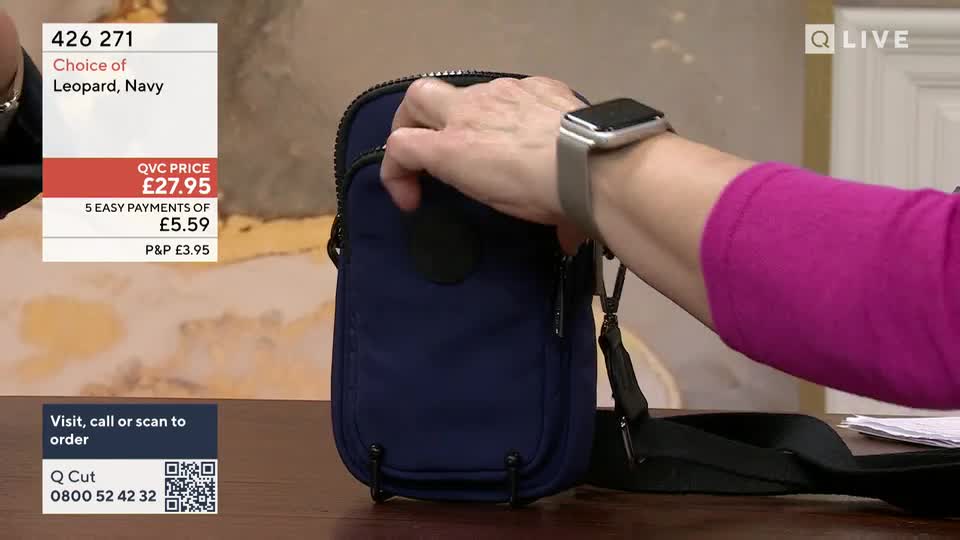 A hand reaches into a navy blue bag, its zipper glinting. The bag hangs from a black strap, ready to be shown off.