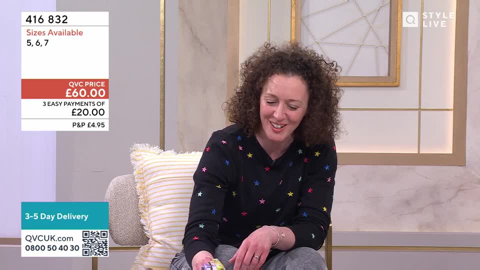 A woman with curly hair smiles as she holds a small, colourful object. On the screen, the QVC price of £60.00 is displayed, alongside delivery information.