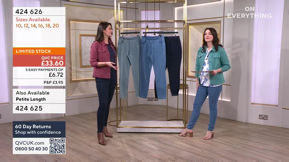 A presenter gestures towards a rack of three pairs of women's trousers, one in a muted green, another in a light blue, and the third in dark navy. Another presenter stands to the right, holding a tablet and wearing a similar outfit.