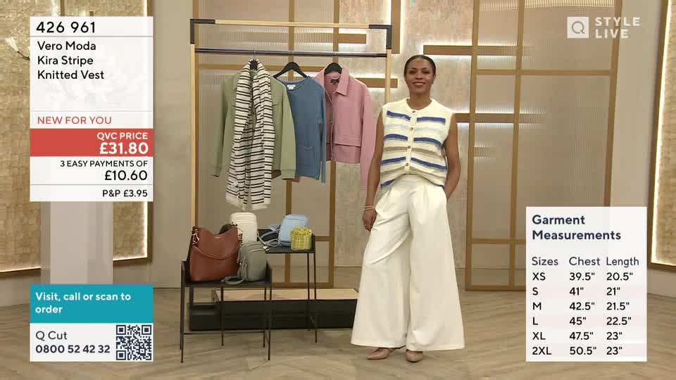 A woman stands in wide-leg cream trousers and a striped knitted vest. On a rack behind her, a pale green jacket and a pink jacket hang next to a blue jumper.