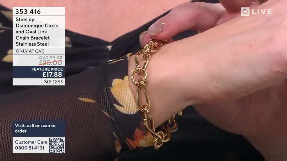 Fingers adjust a gold bracelet with oval and circular links. The bracelet gleams against a dark, floral-patterned sleeve.