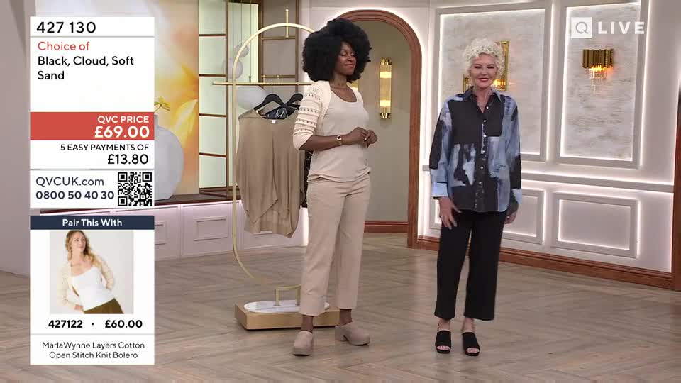 Two women stand on a brightly lit set, presenting clothing. The woman on the left wears a beige knit bolero and trousers, while the woman on the right sports a patterned shirt and black pants.