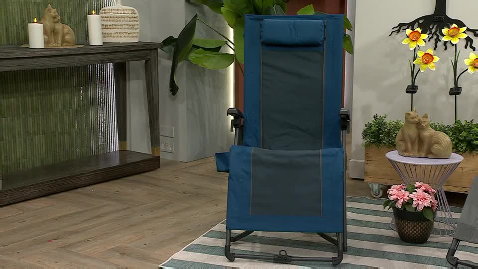 A teal and grey recliner chair stands center stage, framed by decorative items like candles and a cat sculpture. The set looks like it's from a QVC segment, somewhere in the United Kingdom.
