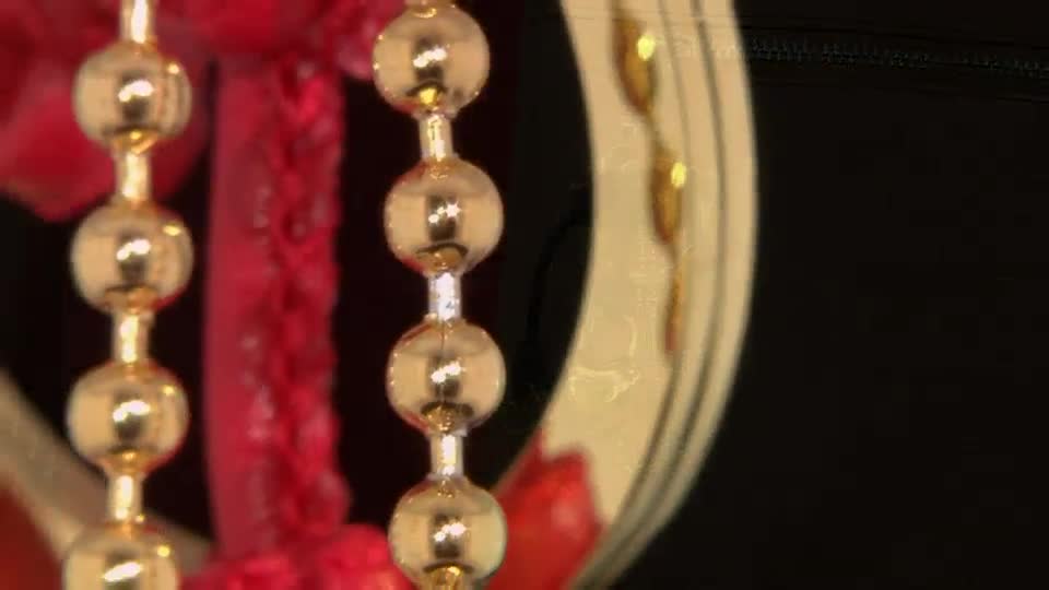Shiny gold beads hang in a vertical line, reflecting the light. A red tassel is visible next to them, and a curved gold rim is on the right.

