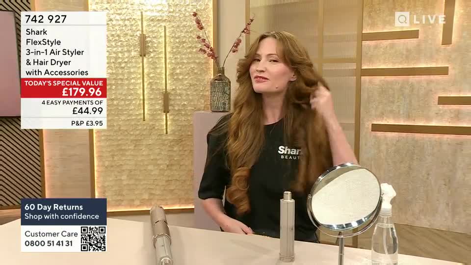 A woman on QVC in the United Kingdom is demonstrating a hair styling tool, running her fingers through her long, wavy hair. The product's price is displayed on the screen, along with a customer care number.
