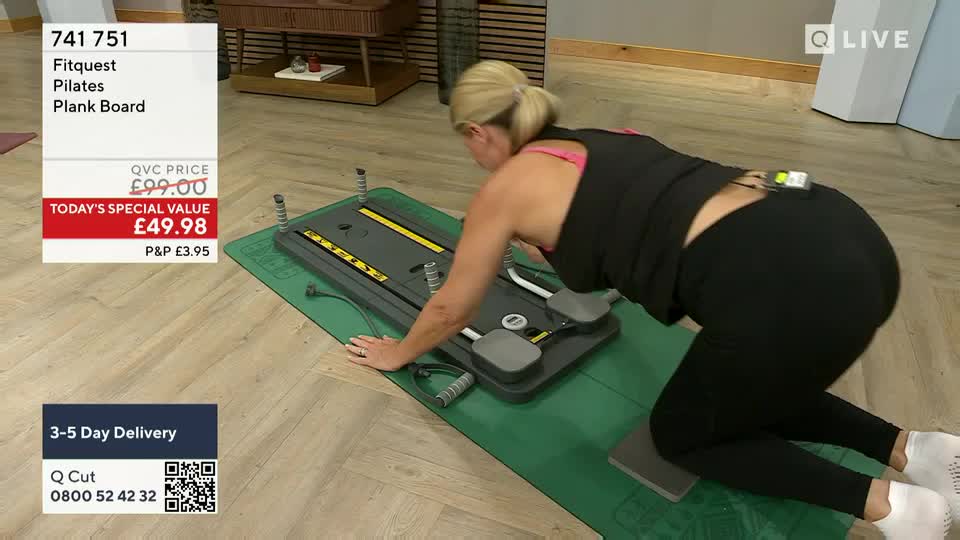 On a green mat, a woman in black leggings and a tank top is demonstrating a plank board, her hands and knees positioned on the equipment. She's on QVC in the United Kingdom, and the price of the "Fitquest Pilates Plank Board" is displayed on the screen.
