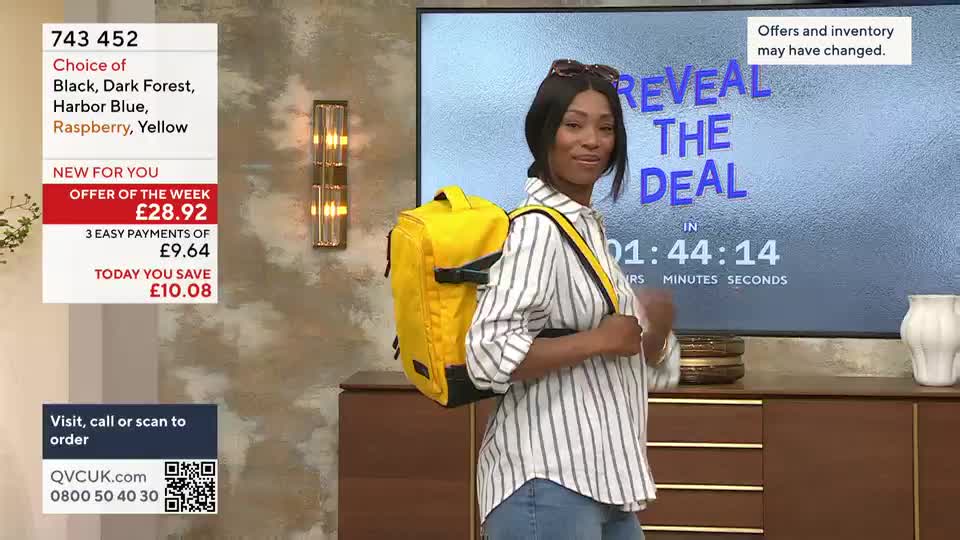 A woman in a striped shirt and jeans is modeling a bright yellow backpack on a QVC set. A timer counts down on a screen behind her, and the on-screen text advertises a deal.

