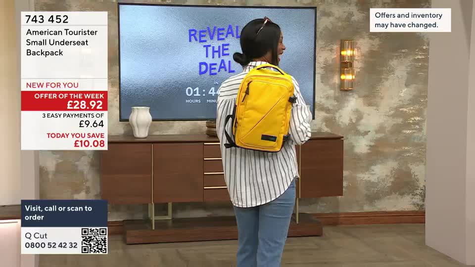 A woman in a striped shirt stands with a bright yellow backpack on her back, facing away from the camera. On a screen behind her, a countdown timer ticks down during a QVC segment.
