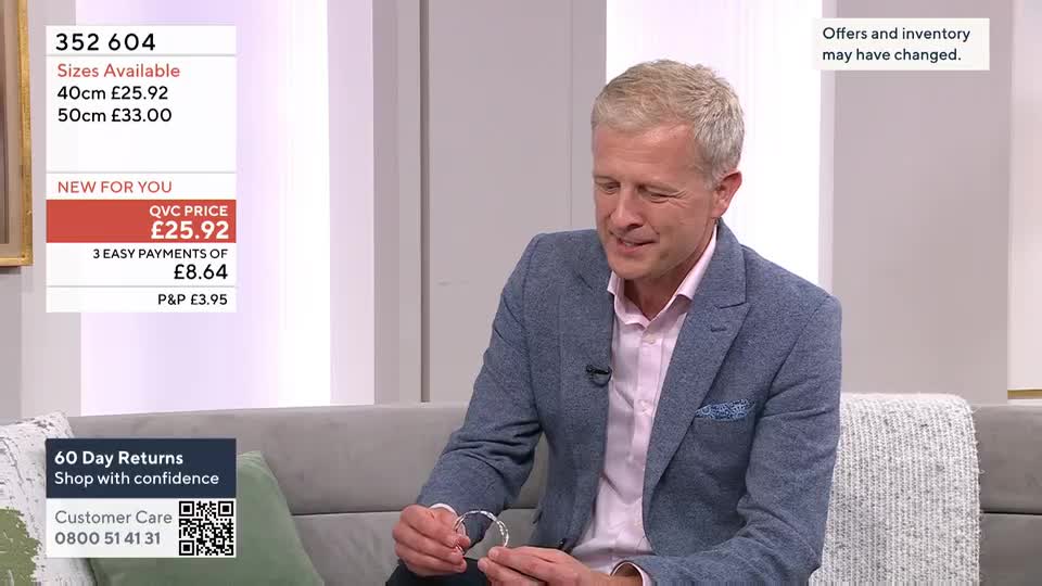 A man in a blazer holds a silver bracelet, turning it gently in his hands. On the screen, a QVC price of £25.92 is displayed alongside details about the item.
