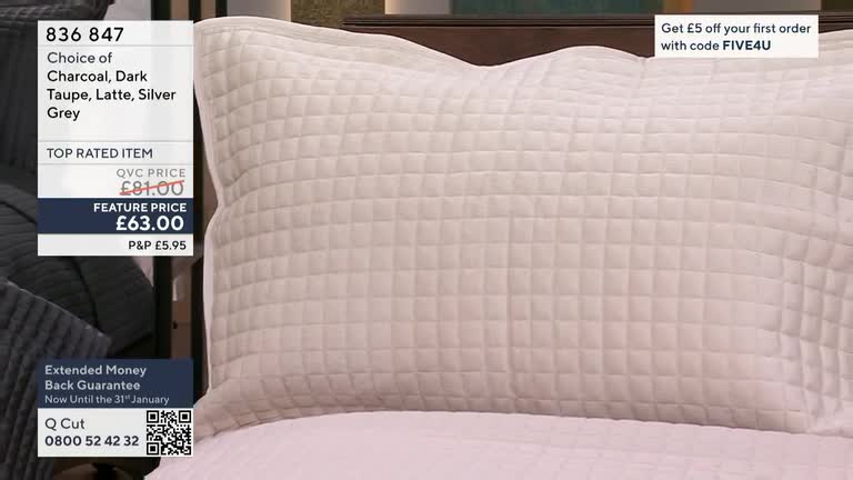 A large, quilted pillow sits on a bed, its neutral color illuminated by studio lights. The QVC price and feature price are displayed alongside the product, a top-rated item.
