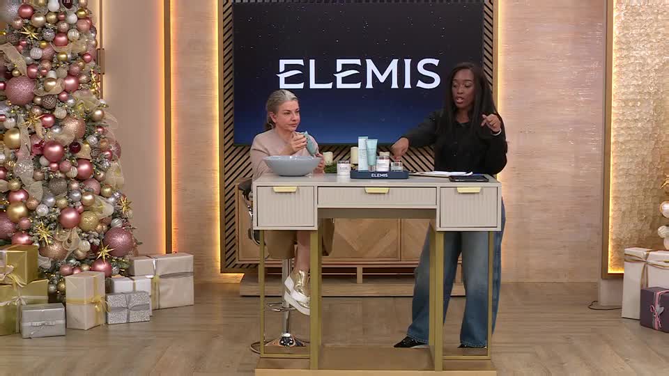 On a QVC set in the UK, a woman in a black top gestures towards skincare products on a desk. Her co-host, seated, holds a small bowl and looks towards the camera.
On a QVC set in the UK, a woman in a black top gestures towards skincare products on a desk. Her co-host, seated, holds a small bowl and looks towards the camera.