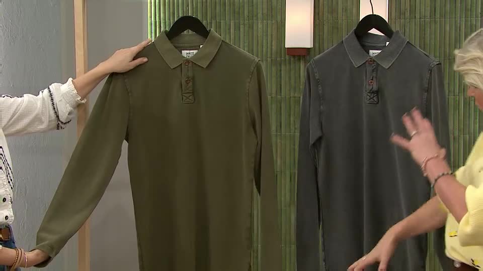 A hand reaches out to touch the shoulder of a deep olive green long-sleeved polo shirt. Beside it, another woman gestures towards a charcoal grey version of the same shirt.