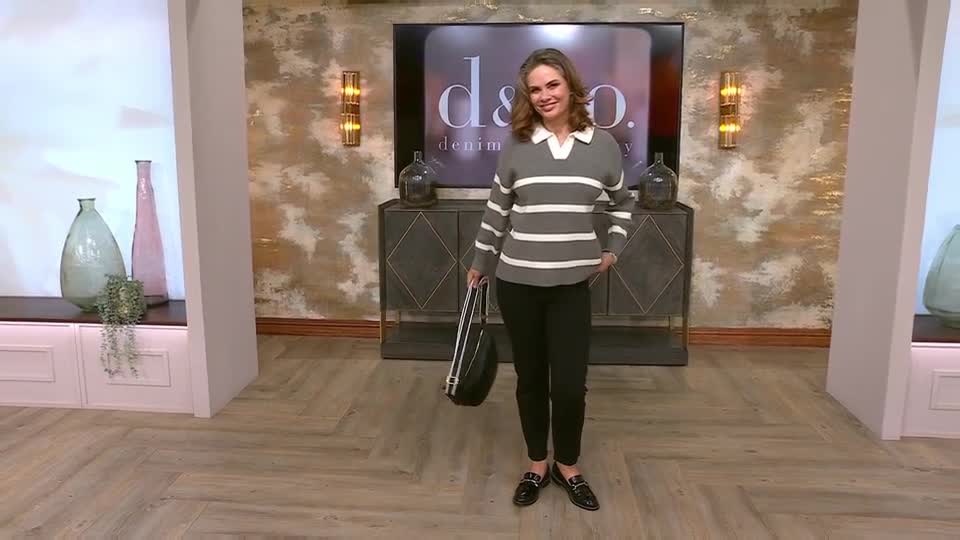 A woman stands on a studio set, presenting a grey and white striped jumper. She holds a black handbag, ready to showcase it. A woman stands on a studio set, presenting a grey and white striped jumper. She holds a black handbag, ready to showcase it.