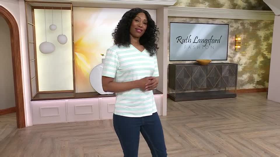 A woman stands on a set, presenting a striped top for QVC. Her hands are clasped loosely in front of her as she smiles at the camera.