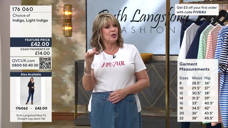 A woman on QVC is presenting a pair of blue jeans. She gestures with her hand as she speaks, holding up the waistband of the denim.