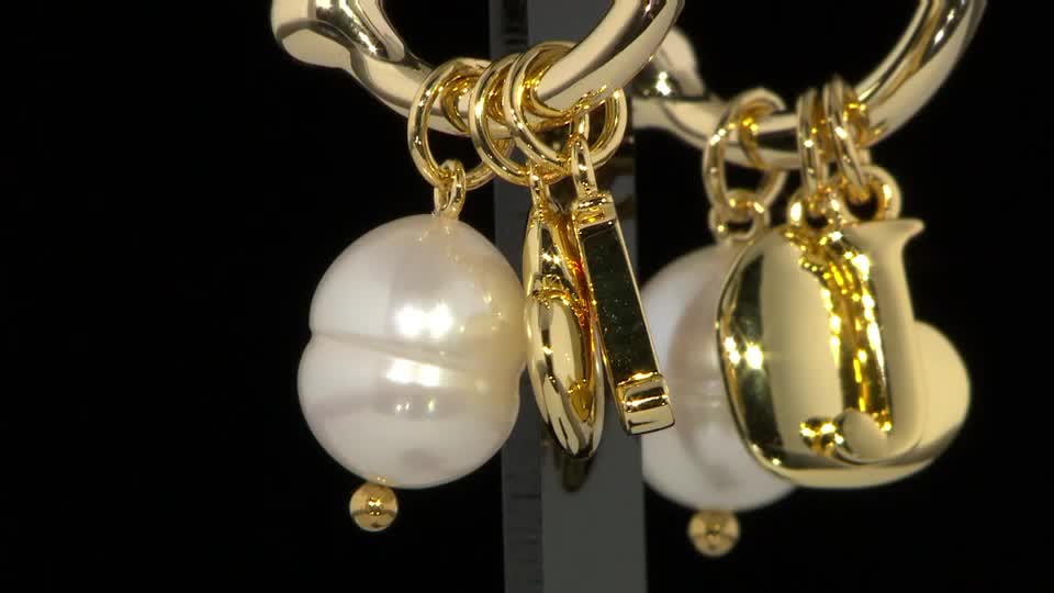 A gold chain dangles several charms, including two large, irregular pearls and a shiny gold letter "J." The pearls catch the light as they sway gently.