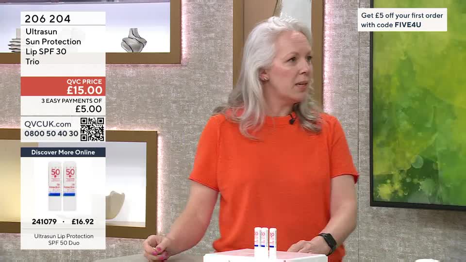 A woman in an orange top is presenting Ultrasun lip protection on QVC. Three lip balm tubes stand upright on a white surface in front of her.