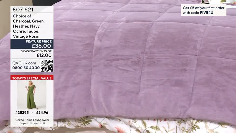 A woman in a green jumpsuit stands on a white background, showcasing a loungewear item. The QVC branding and product details are displayed to her left, with a soft, quilted lilac blanket filling the rest of the frame. A woman in a green jumpsuit stands on a white background, showcasing a loungewear item. The QVC branding and product details are displayed to her left, with a soft, quilted lilac blanket filling the rest of the frame.