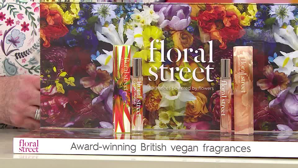 A hand with a silver ring gestures towards a display of Floral Street perfumes. The bottles and their boxes are arranged in front of a vibrant floral backdrop, advertising award-winning British vegan fragrances. A hand with a silver ring gestures towards a display of Floral Street perfumes. The bottles and their boxes are arranged in front of a vibrant floral backdrop, advertising award-winning British vegan fragrances.