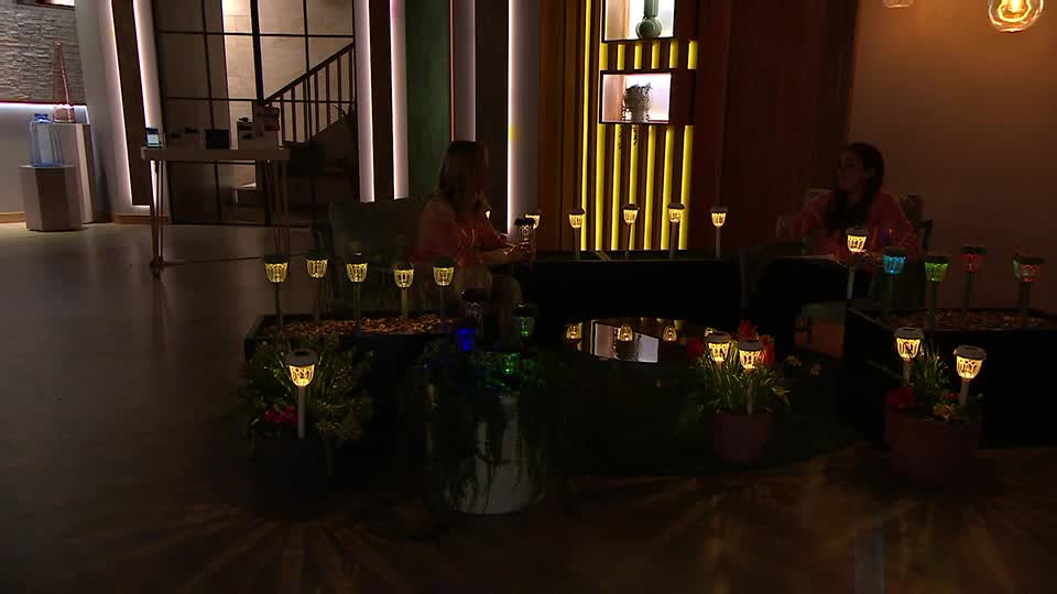 Two women are sitting on a sofa, surrounded by an array of solar-powered garden lights. The lights cast warm yellow and some coloured glows onto the floor. Two women are sitting on a sofa, surrounded by an array of solar-powered garden lights. The lights cast warm yellow and some coloured glows onto the floor.