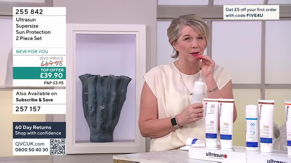A woman on QVC holds a white spray bottle, bringing it close to her mouth. Several tubes of Ultrasun sun protection sit on display in front of her. A woman on QVC holds a white spray bottle, bringing it close to her mouth. Several tubes of Ultrasun sun protection sit on display in front of her.