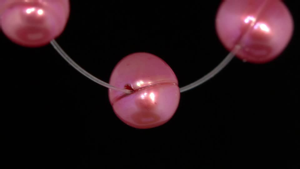 A string of pink pearls, probably from a QVC segment, is threaded onto clear fishing line. The pearls appear to be moving slightly, creating a gentle sway.