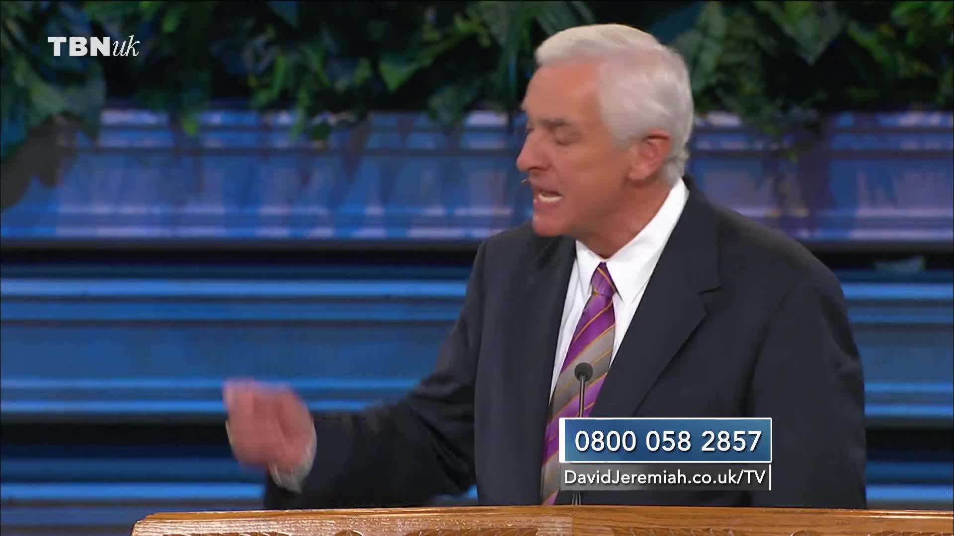 A man in a suit and tie gestures with his left hand, speaking passionately from behind a podium. The TBN UK logo is visible in the corner, along with a phone number and website address.
