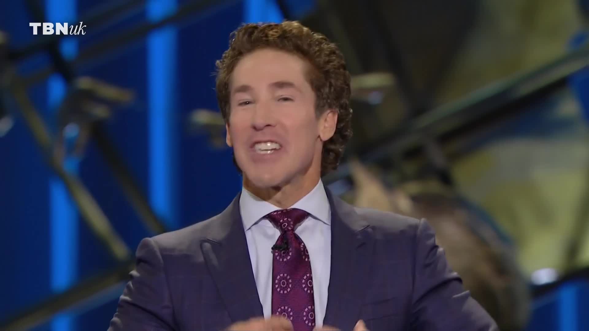 The man in the suit is speaking, his hands moving gently. The TBN UK logo is visible in the corner of the screen.
