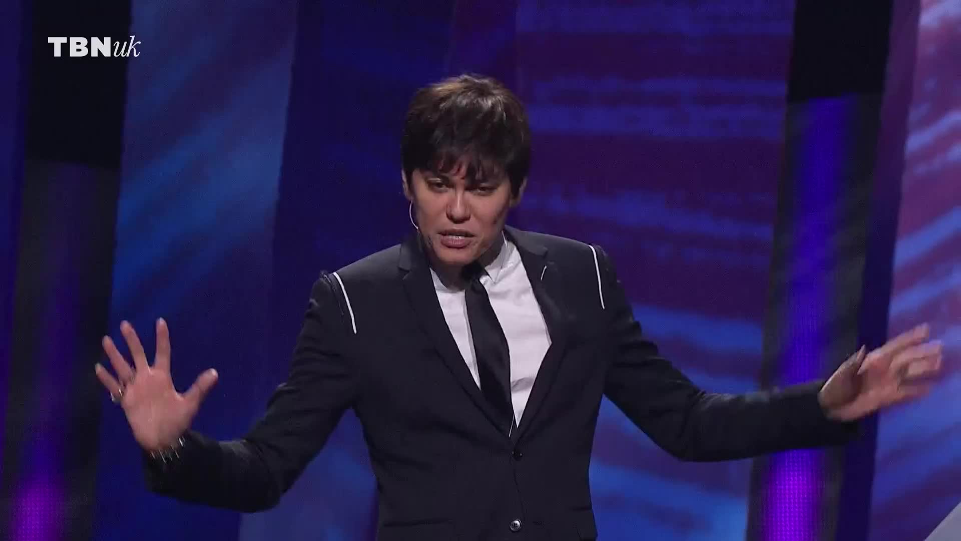 A man in a dark suit gestures with both hands, his expression animated. The TBN UK logo is visible in the corner, suggesting this is a broadcast from the United Kingdom.
