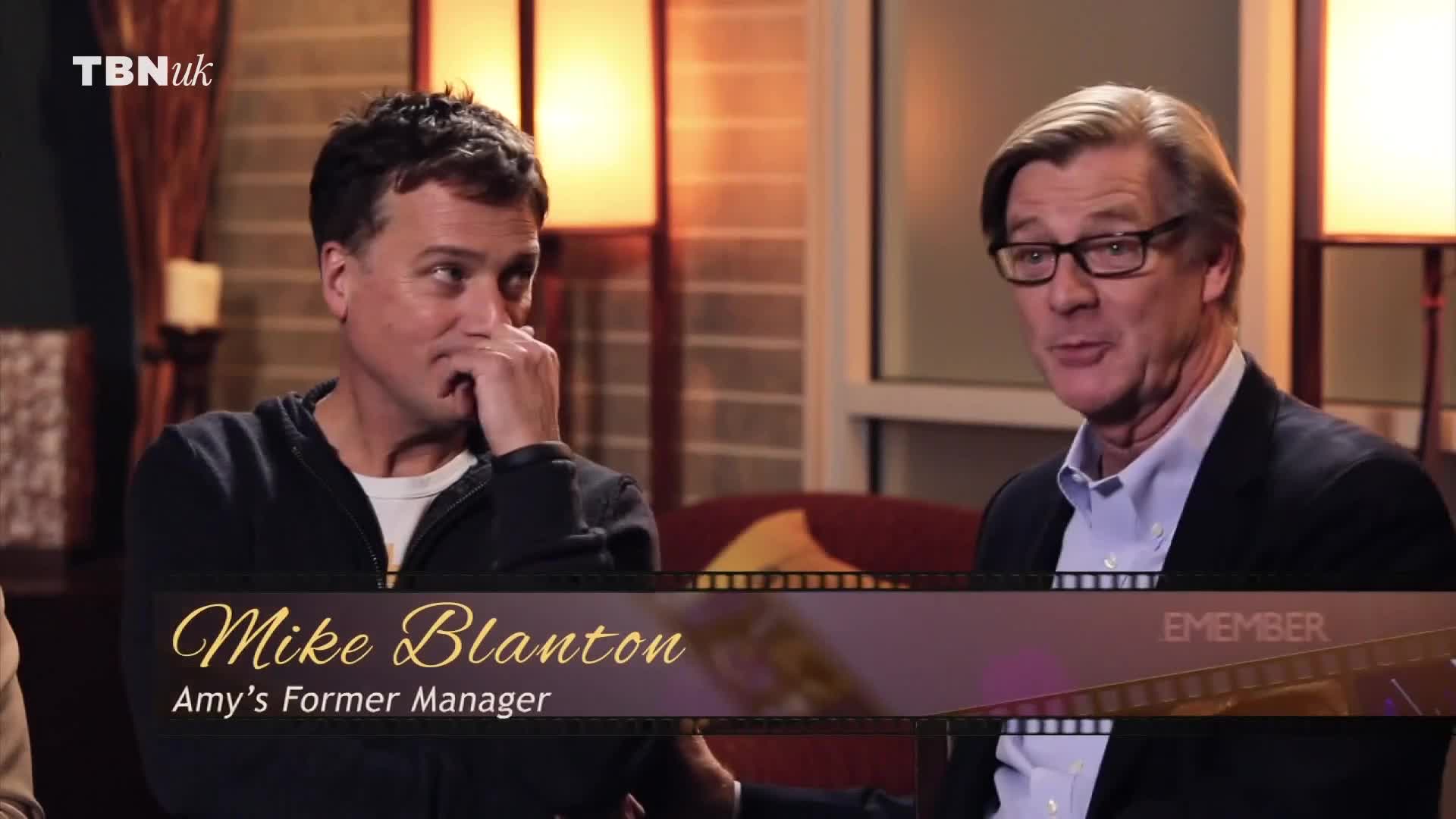 One man, identified as Amy's former manager, wipes his eye, while another, wearing glasses, speaks with a slight smile. The TBN UK logo is visible in the corner.
One man, identified as Amy's former manager, wipes his eye, while another, wearing glasses, speaks with a slight smile. The TBN UK logo is visible in the corner.