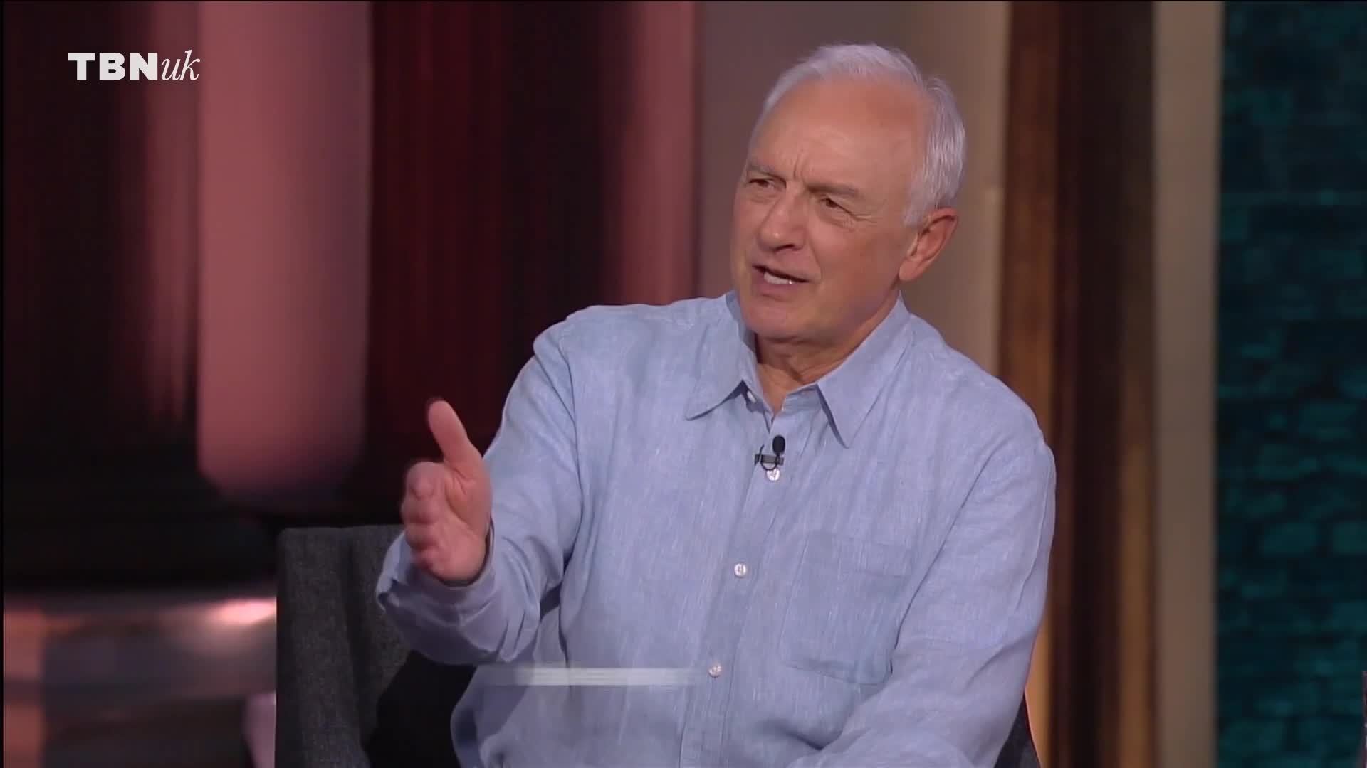 A man in a blue shirt gestures with his right hand, speaking on a TBN UK set. His other hand is up, thumb extended, as he makes his point.
A man in a blue shirt gestures with his right hand, speaking on a TBN UK set. His other hand is up, thumb extended, as he makes his point.