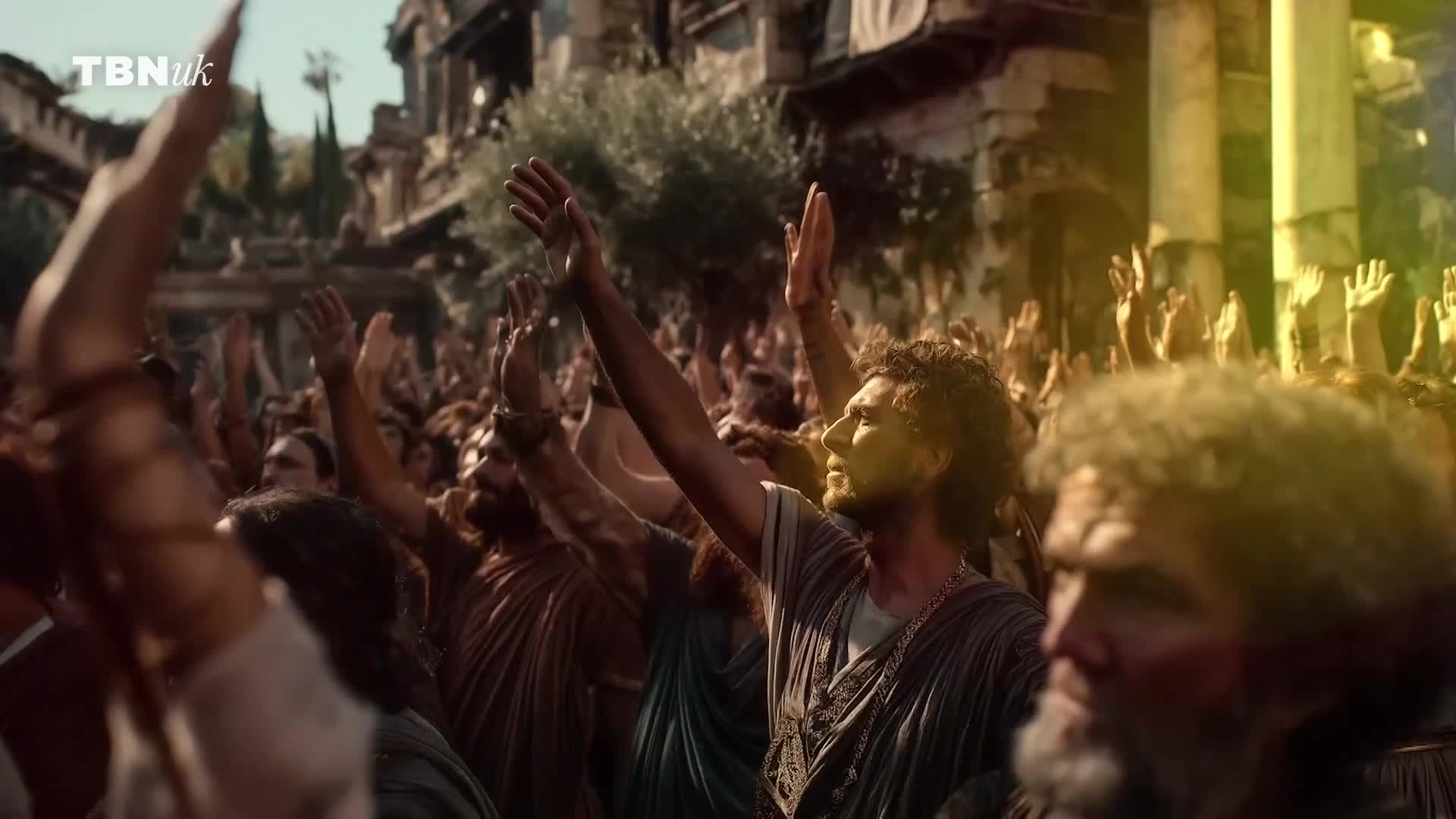 A crowd of people in ancient-style clothing raise their arms in unison. The scene, likely from a TBN UK production, seems to be set in a public square.
A crowd of people in ancient-style clothing raise their arms in unison. The scene, likely from a TBN UK production, seems to be set in a public square.