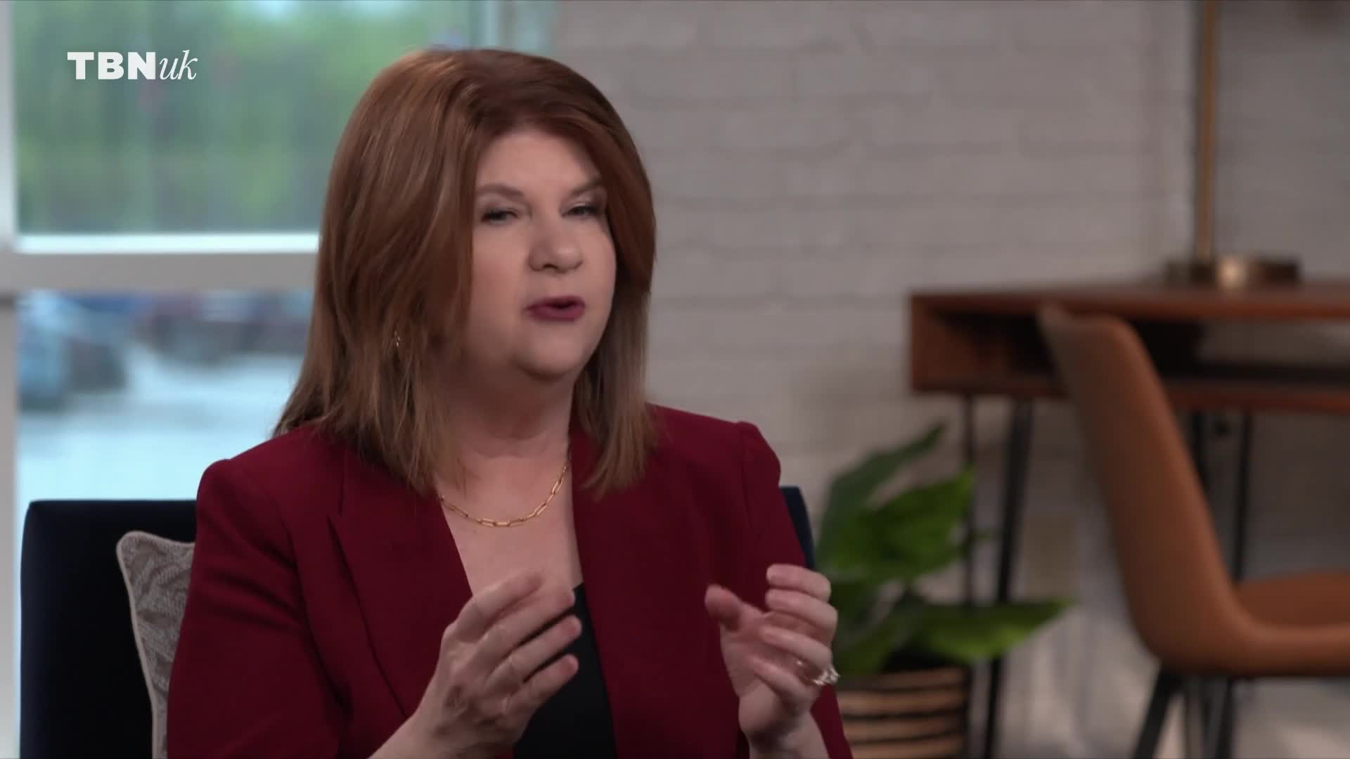 A woman in a red blazer speaks with her hands animatedly. The TBN UK logo appears in the top left corner.