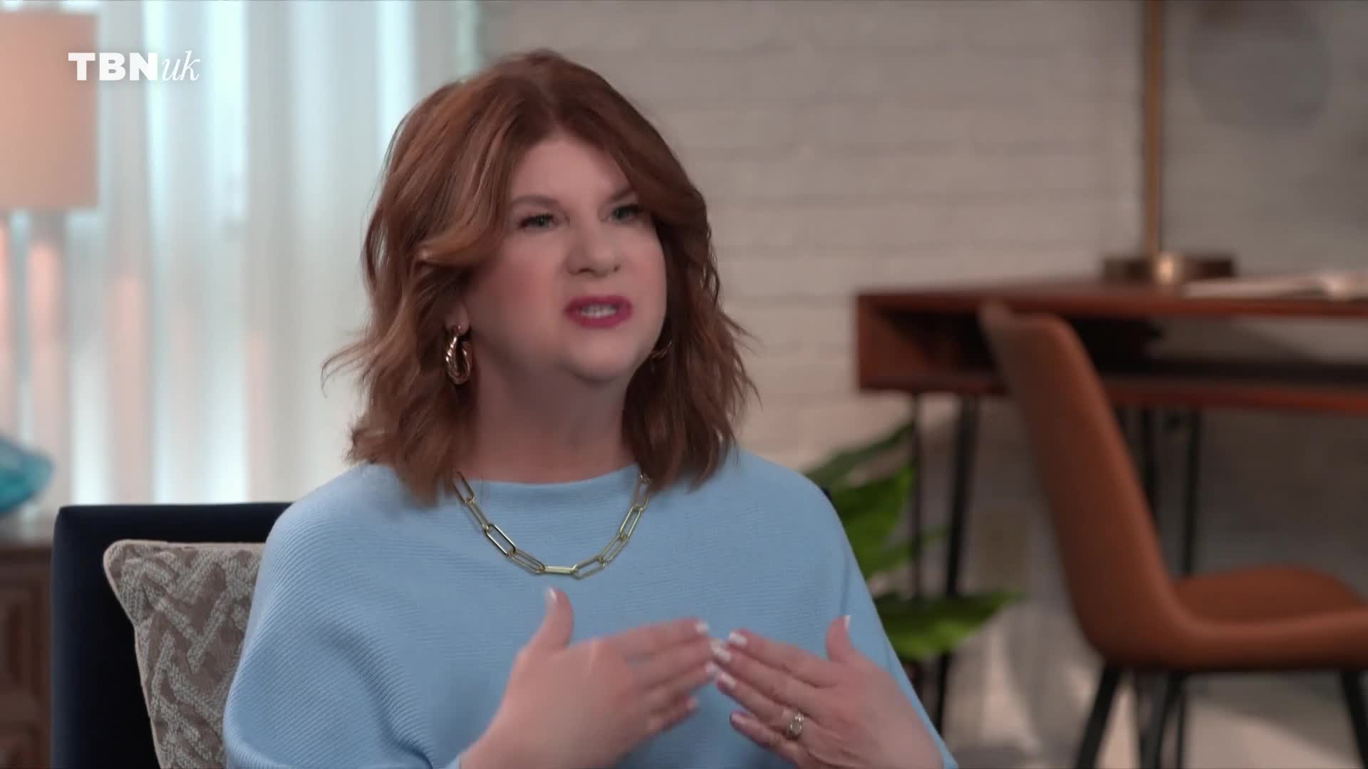 A woman with auburn hair is speaking animatedly, gesturing with her hands. The TBN UK logo appears in the upper left corner of the screen.