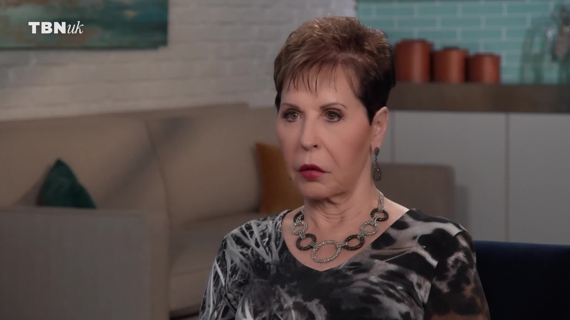 A woman with short brown hair and a patterned top looks intently forward. A TBN UK logo appears in the top left corner of the frame.